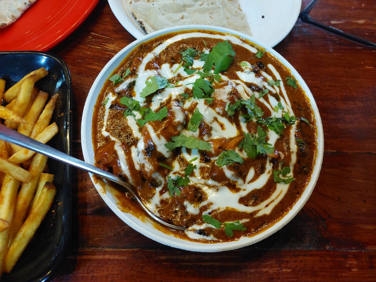 Bowl of butter chicken curry with rice and fries